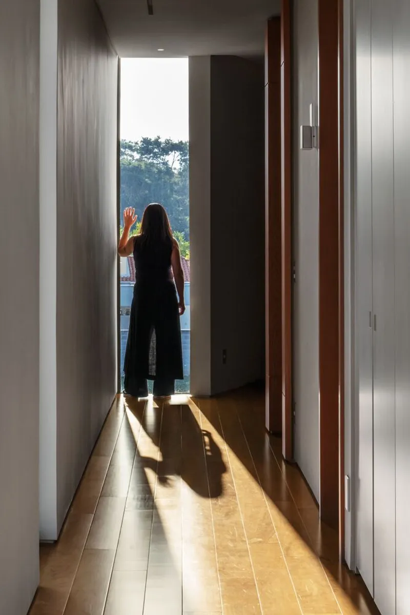 Woman standing in a wood-floored corridor with floor lighting looking toward the landscape