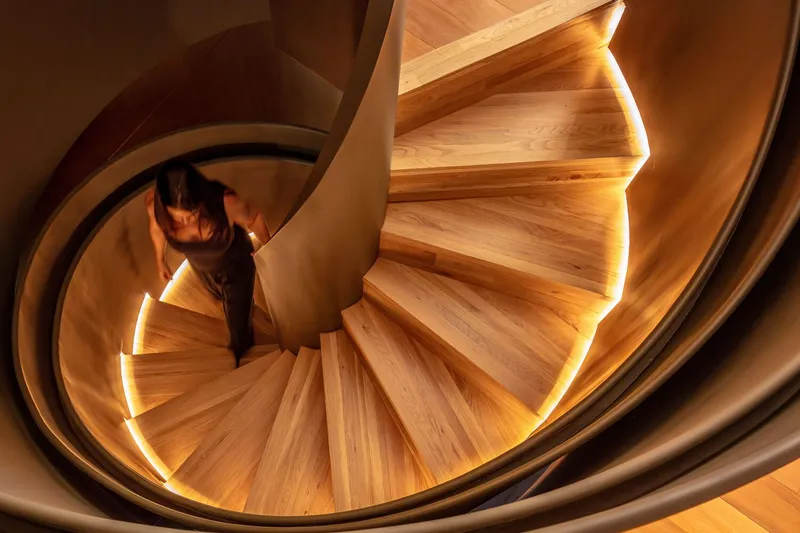 Overhead view of timber spiral staircase with integrated LED lighting and a person ascending