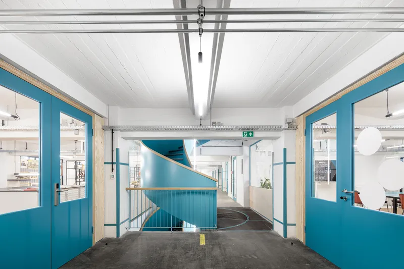 Spiral staircase with turquoise cladding viewed through a corridor with blue painted door frames