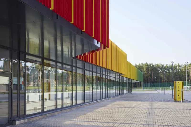 Full-height glazed corridor below stacked red and yellow vertical corrugated metal panels with yellow signage box