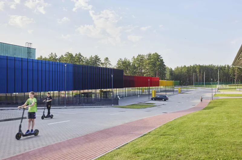 View of multicolored metal panel facade with children riding scooters on adjacent path at dusk