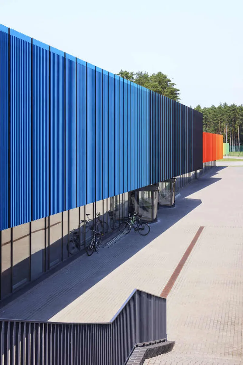 Elevated walkway beneath blue vertical metal cladding with bicycles parked along the ground level