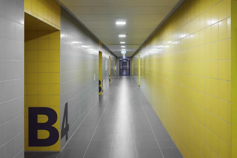 Long corridor with yellow and grey tiled walls, grey floor, and recessed ceiling lighting