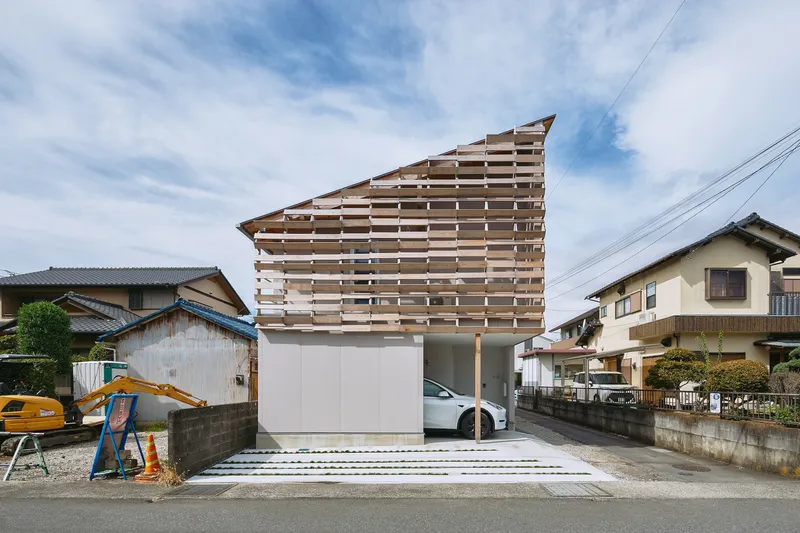 Street view of the horizontal timber louvre facade rising above a white garage base and driveway