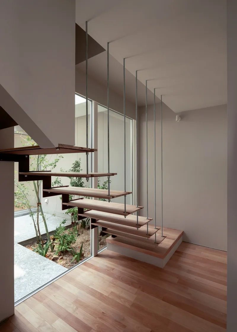 Floating timber treads with steel rod suspension alongside a glazed courtyard with planted greenery