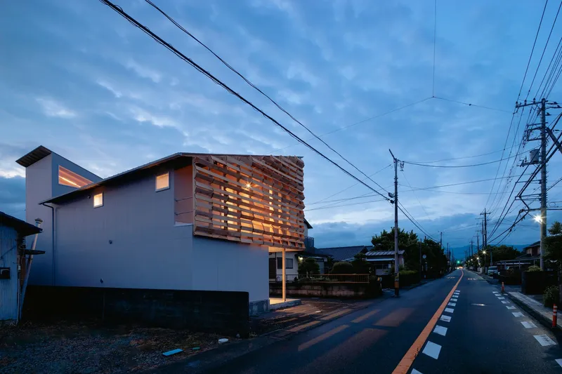 Streetside view at dusk showing the illuminated timber screen facade and overhead power lines