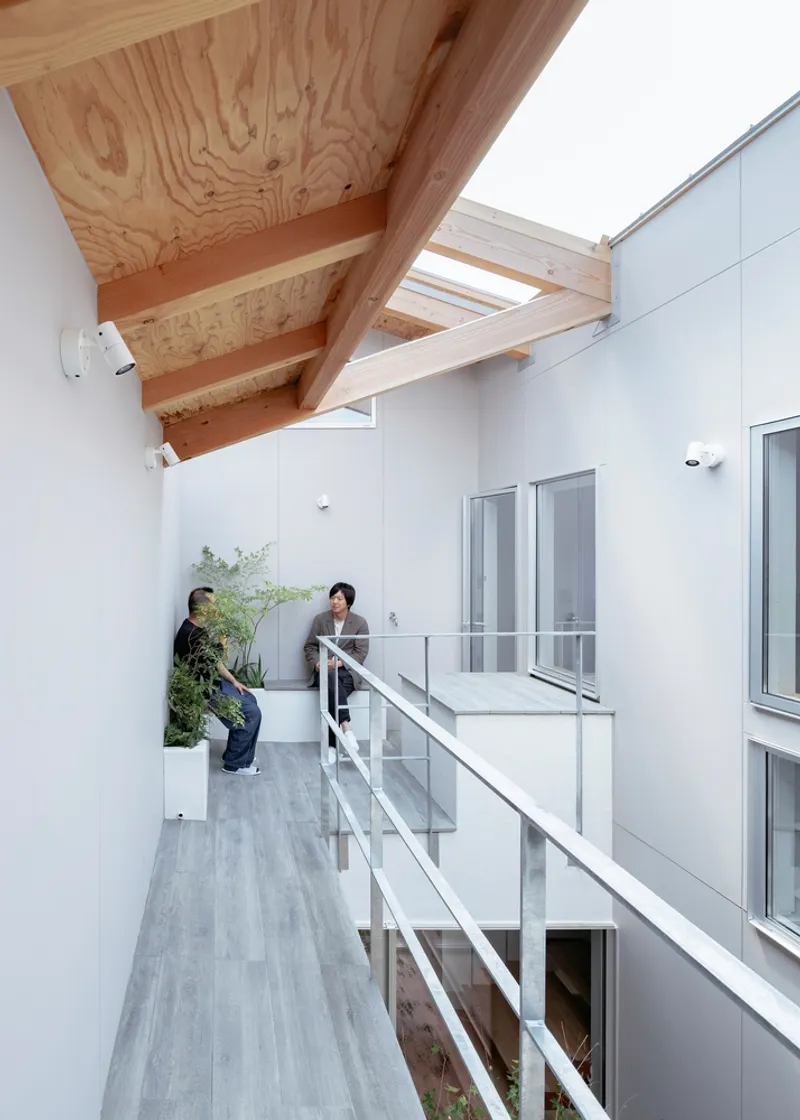 Upper walkway with glass railing and plywood beam roof where two people tend to plants