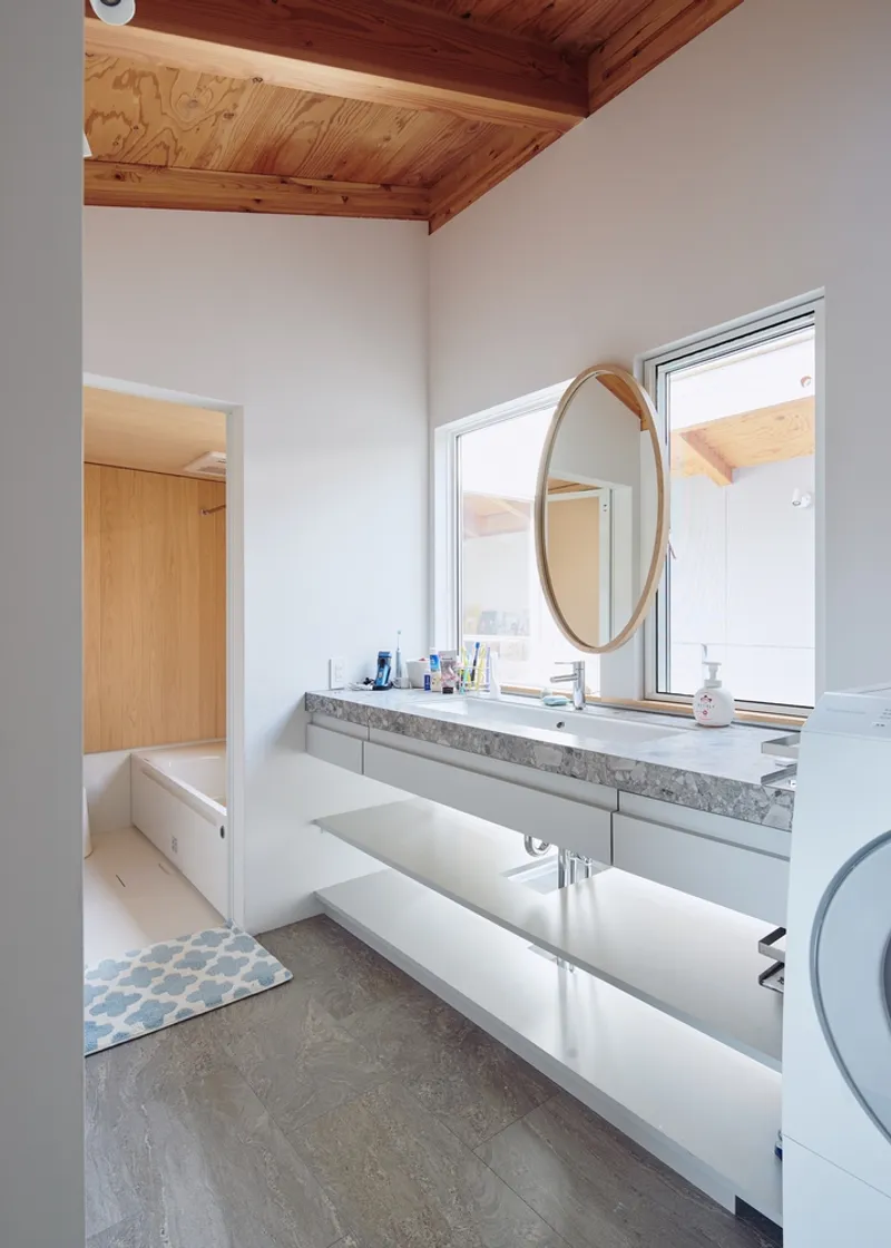 Bathroom with terrazzo vanity counter and round mirror beneath a vaulted timber ceiling