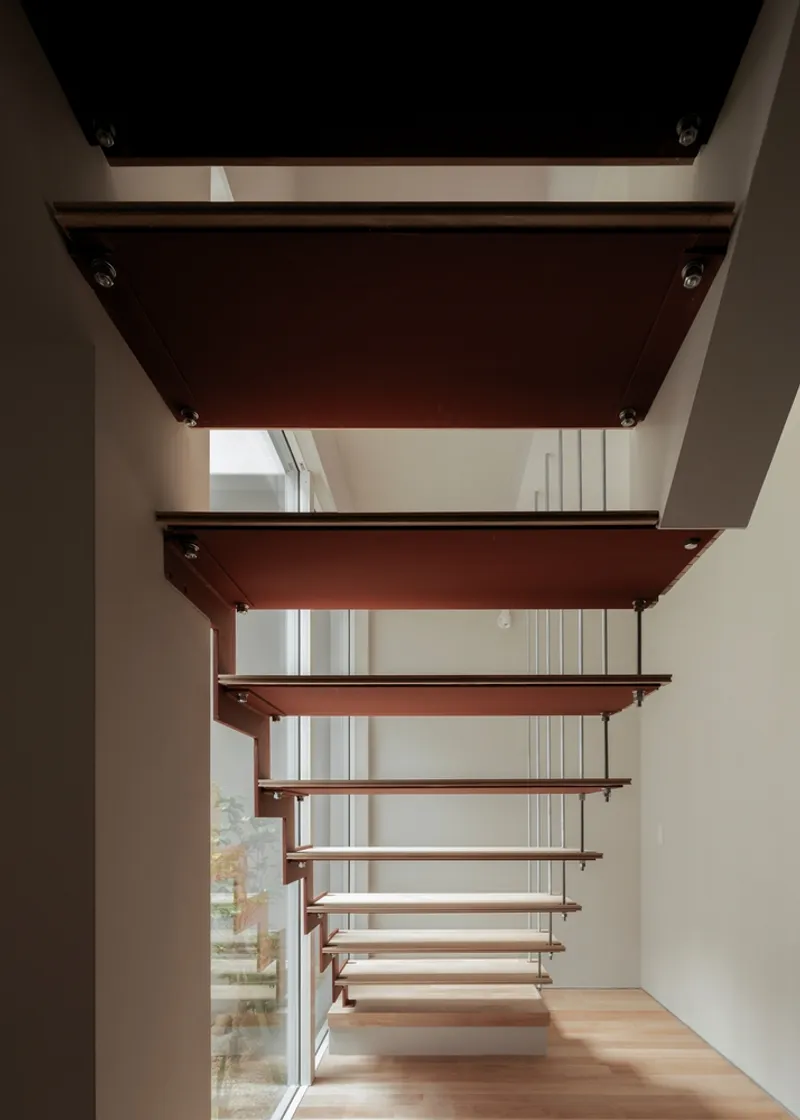 Cantilevered timber stair treads with steel plates suspended between white walls and a tall window