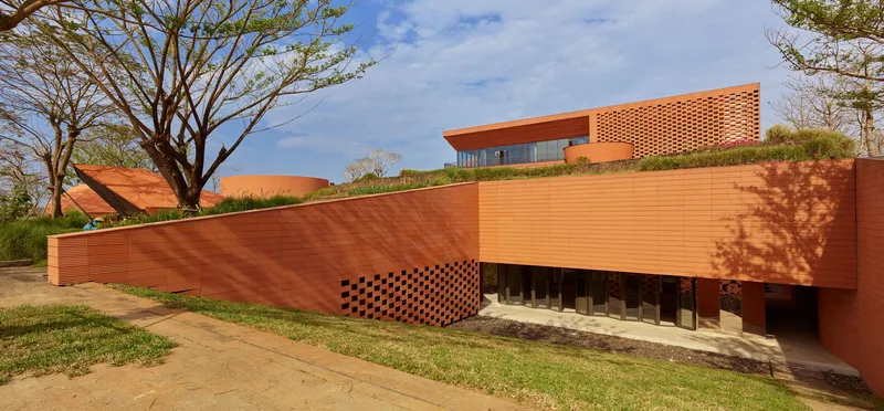 Horizontal ribbed terracotta wall casting tree shadows along a grass embankment in afternoon light