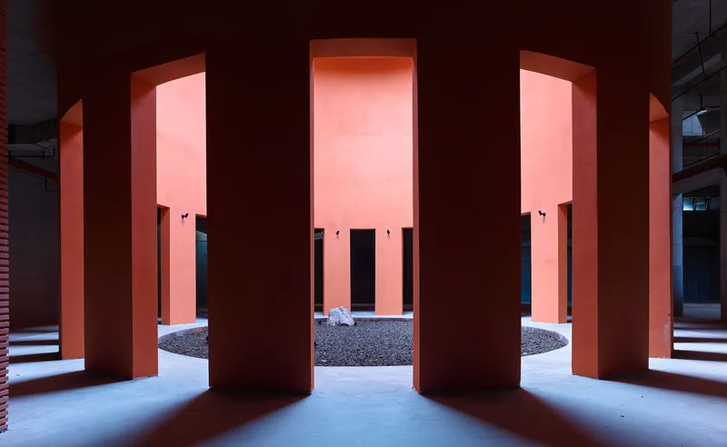 Colonnade of terracotta columns with pink illuminated recesses at dusk