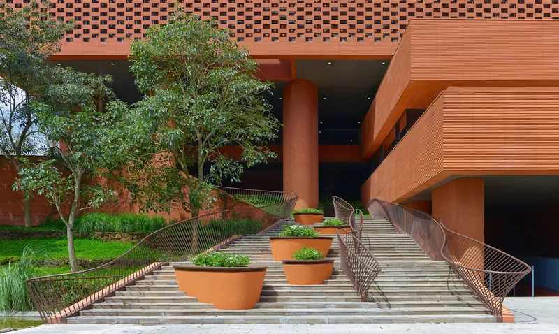 Pedestrian ramp with metal railings and planted terracotta pots flanked by trees in the courtyard