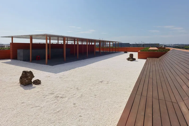 Rooftop terrace with gravel surface, timber decking, rock elements and steel pergola under open sky
