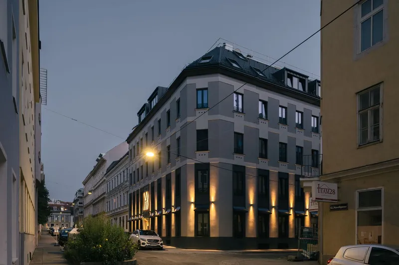 Corner building with illuminated ground floor columns and vertical uplights at dusk