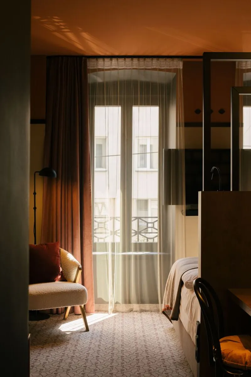 Hotel room interior with floor-to-ceiling curtains filtering warm afternoon sunlight