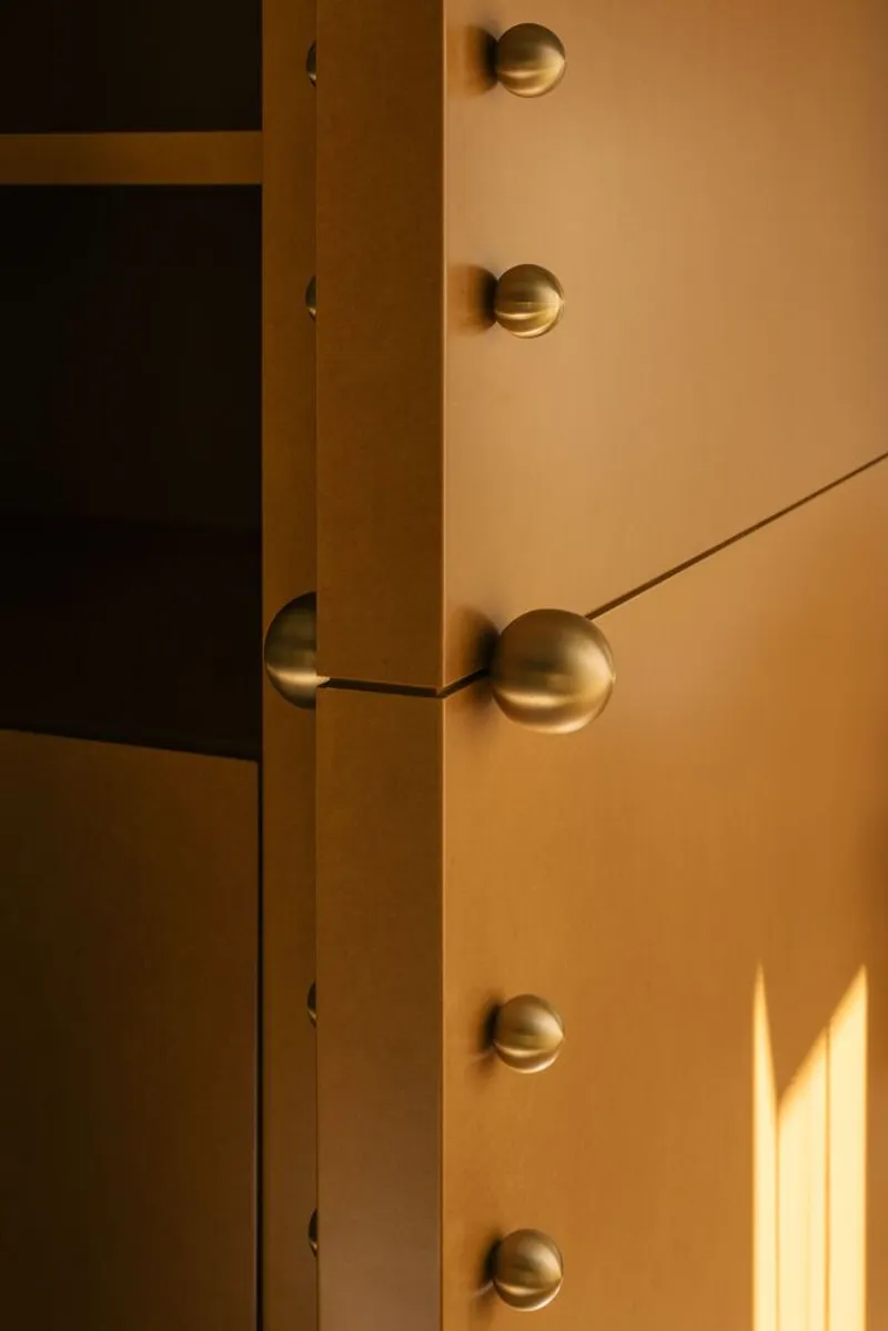 Detail of brass spherical door handle and vertical cabinet hardware in afternoon sunlight
