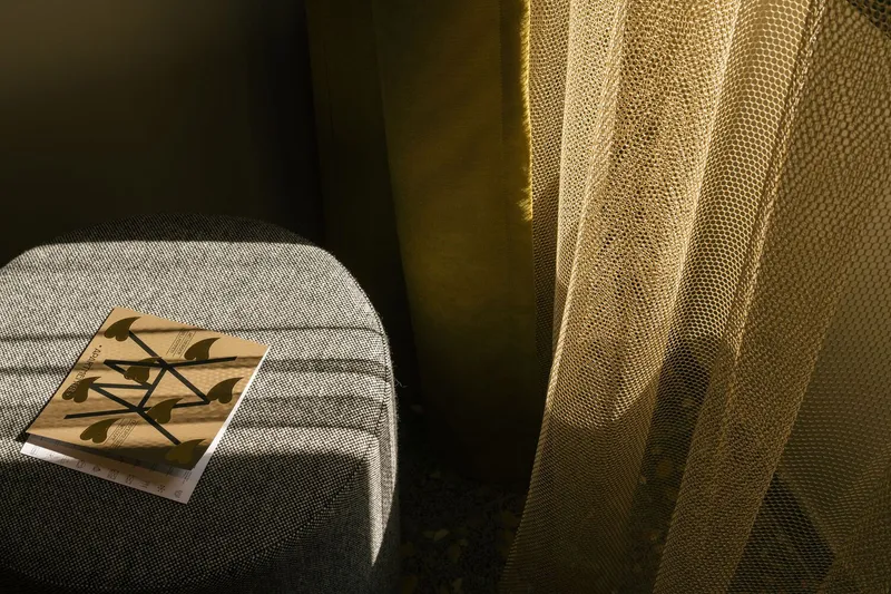 Upholstered chair with book illuminated by sunlight filtering through yellow mesh curtain