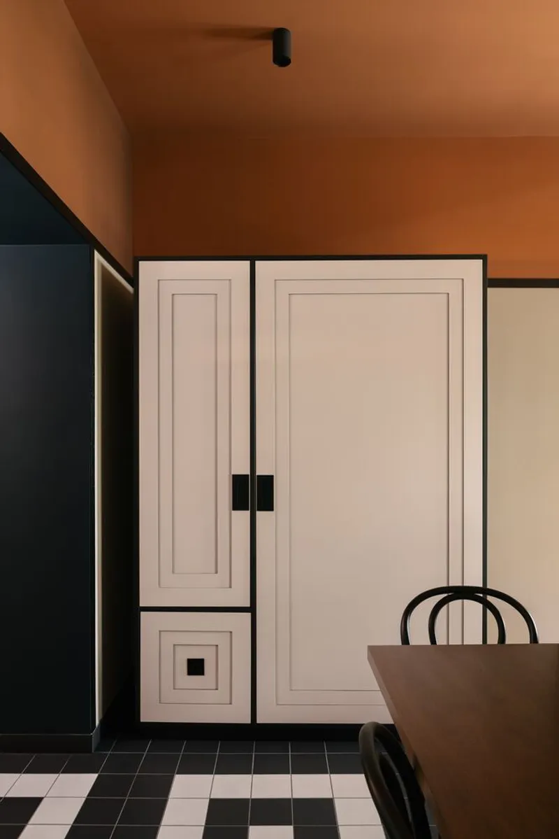 White paneled cabinetry with black hardware against checkered floor tile and orange ceiling plane