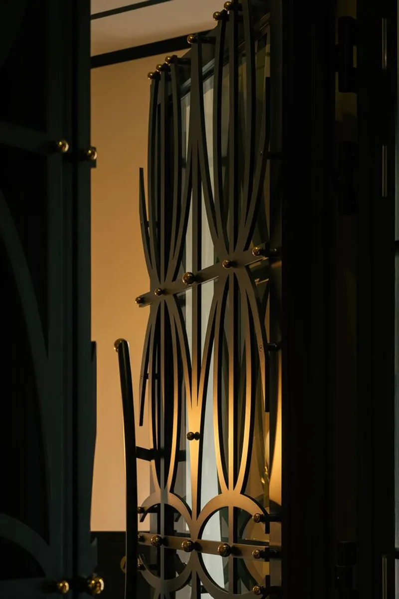 Close-up of decorative metal gate with curving rods backlit by warm interior glow