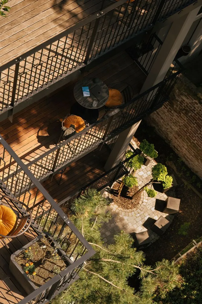Top-down view of tiered outdoor terraces with metal mesh railings, planted beds and afternoon shadows