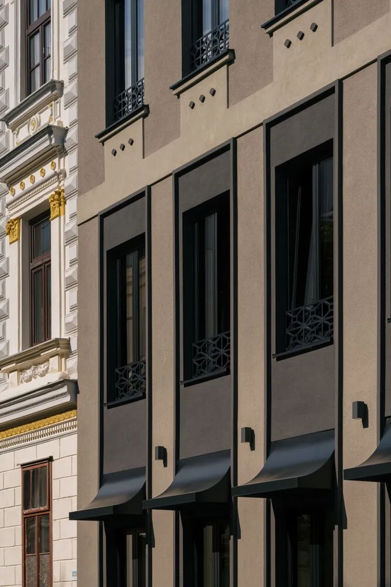 Three projecting bay windows with dark metal frames and patterned balcony railings in afternoon light