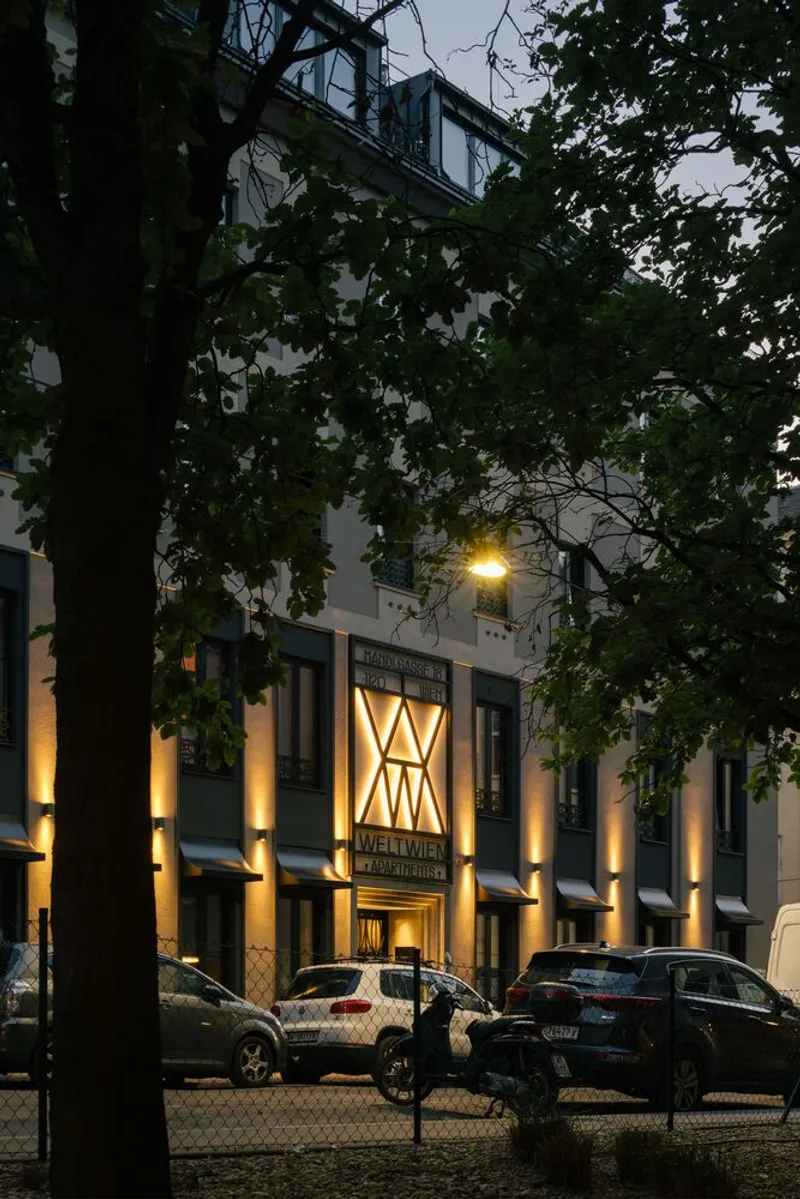 Illuminated facade seen through tree branches at dusk with parked cars along the street
