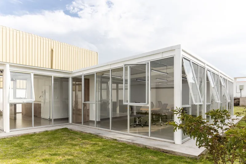 Glass-walled extension with white steel diagonal bracing and concrete patio beneath cloudy sky