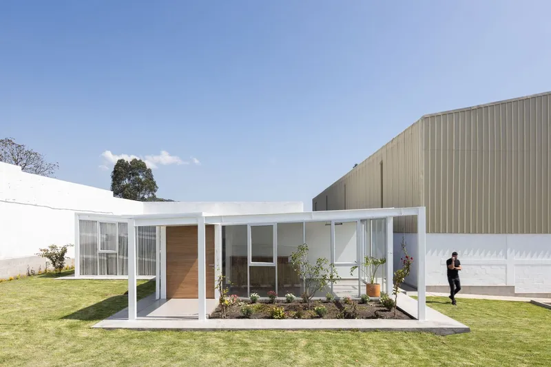 Framed courtyard pavilion with timber entry door and figure walking past the corrugated metal volume