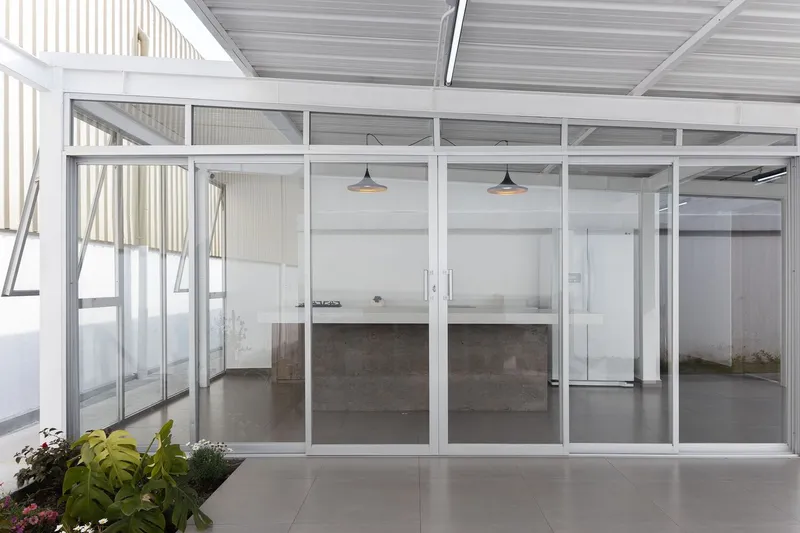Glazed courtyard wall revealing interior kitchen island with pendant lights and polished concrete floor