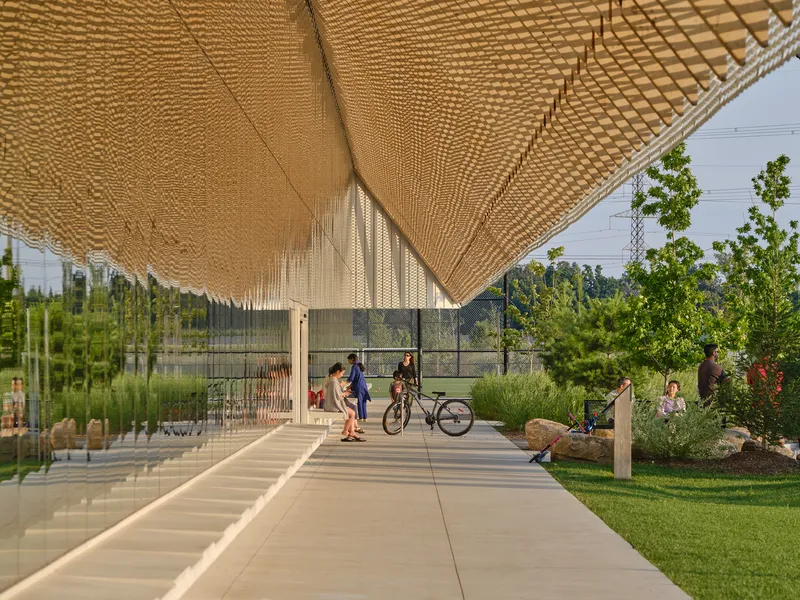 Woven timber canopy over concrete walkway with people cycling through landscaped garden