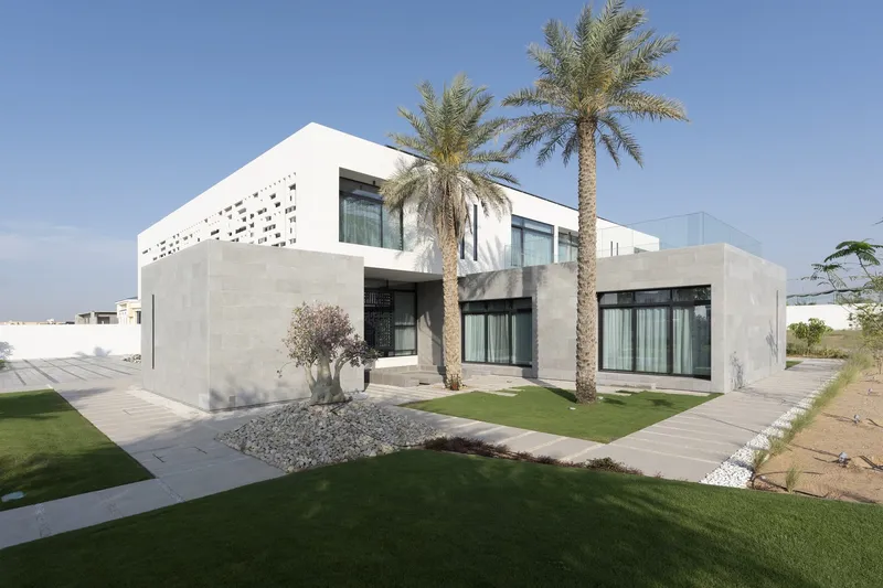 Two-storey concrete and white plaster volumes with perforated upper screen flanked by palm trees and lawn