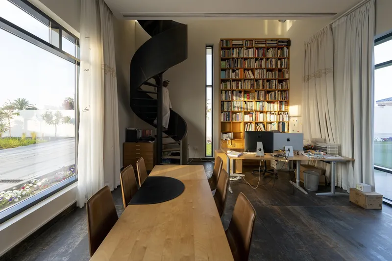 Double-height library space with floor-to-ceiling bookshelf, black spiral stair and long dining table