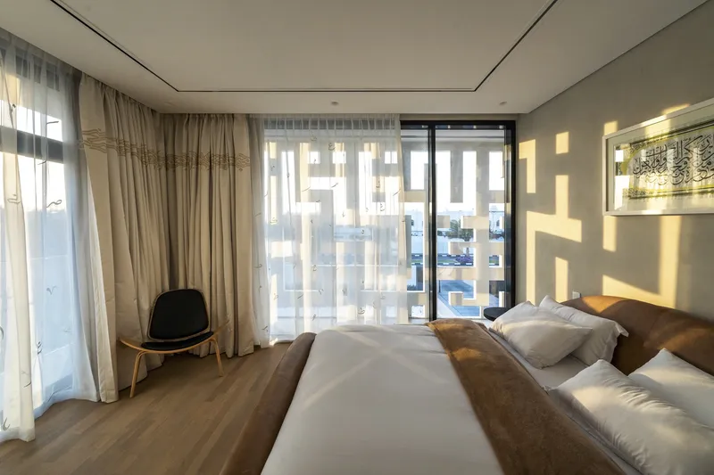 Bedroom with sheer curtains casting geometric screen shadows onto the wall at midday