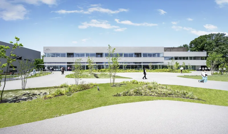 Front facade with horizontal window bands and landscaped courtyard with planted beds and pathways under blue sky