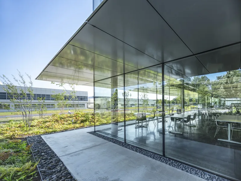 Glass-walled dining area beneath cantilevered canopy with planted beds and pebble borders adjacent to glazed facade