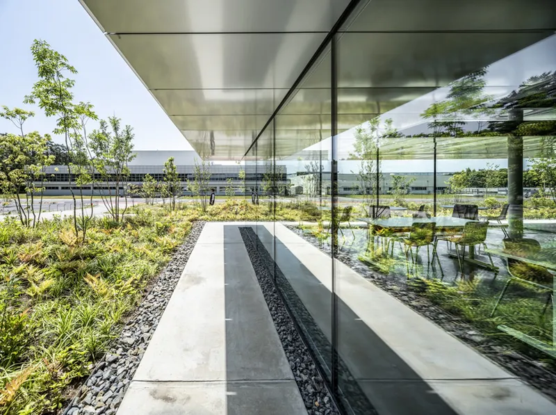 Covered terrace with concrete water channel bordered by black gravel and planted beds with young trees