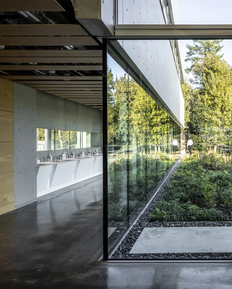 Glass threshold between interior washroom and exterior planted courtyard with person visible outside