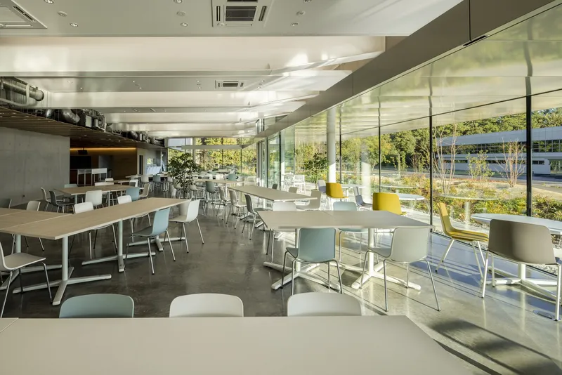 Cafeteria interior with floor-to-ceiling glazing overlooking landscape and polished concrete floors