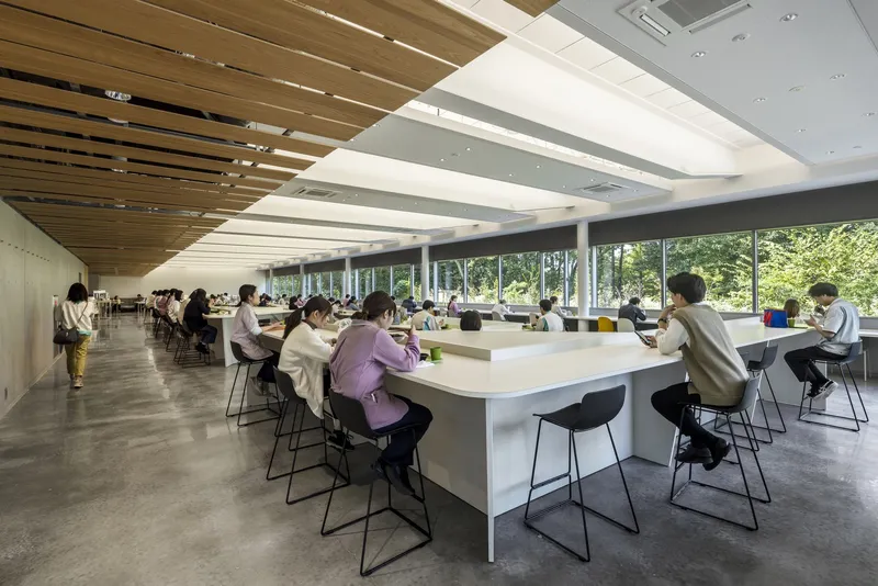 Library reading room with timber ceiling baffles and people seated at long shared tables