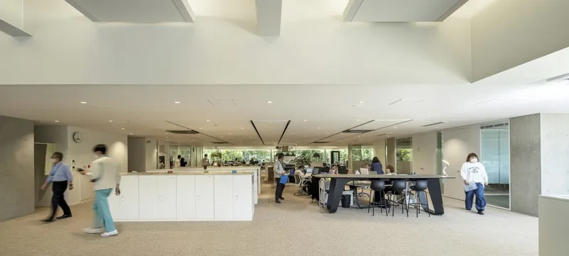 Office breakout area with white storage islands, exposed concrete columns, and staff moving through the carpeted central circulation zone
