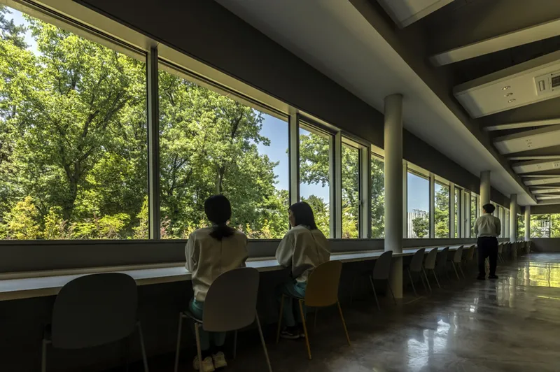 Long reading counter along window wall with two people seated looking toward forest