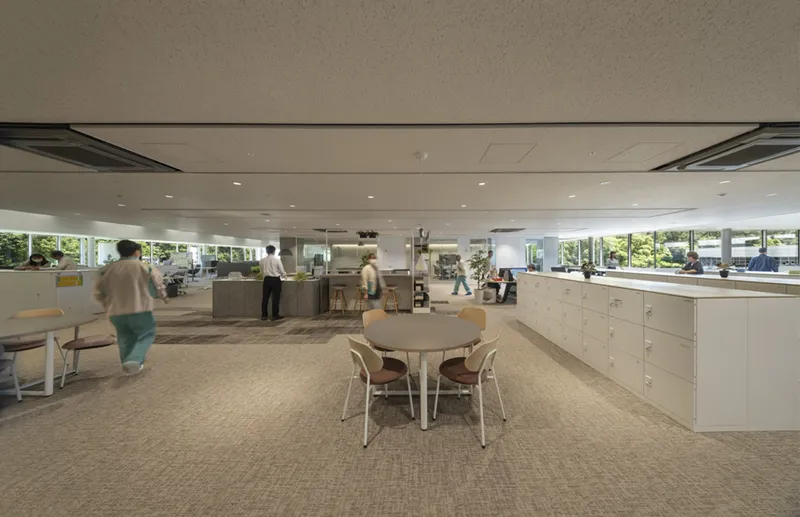 Collaborative workspace with round white table and storage cabinets beneath a suspended ceiling with flush-mounted climate units