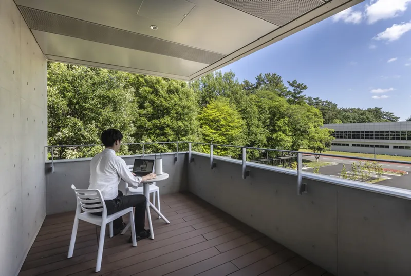 Covered outdoor terrace with timber decking, metal railing, and single occupant working at a small table overlooking the forested landscape
