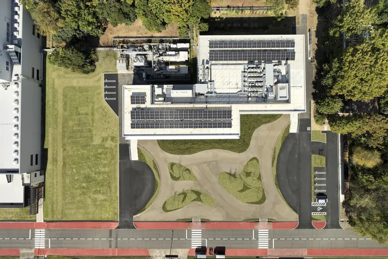 Overhead drone view showing rooftop solar panels and curving garden paths bordered by lawn and trees