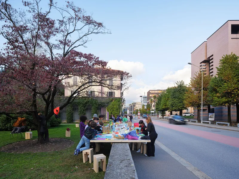 Community table with timber stools on a lawn beside a pedestrian street at dusk