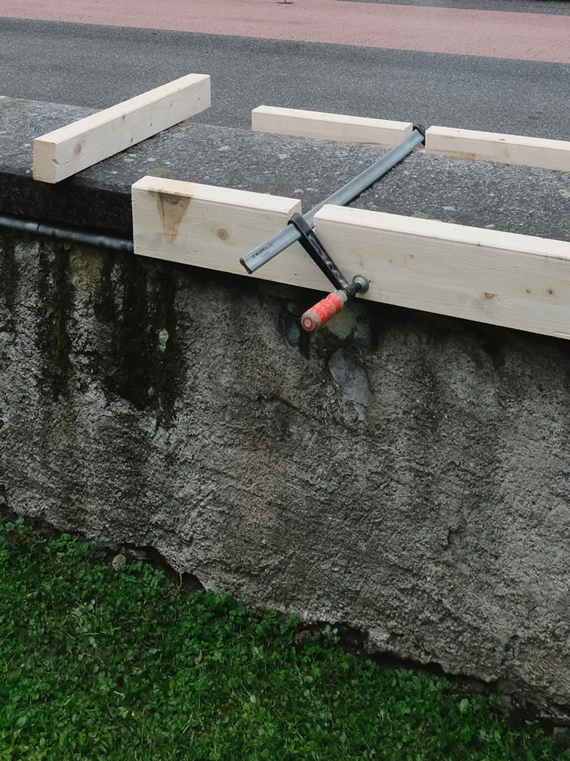 Detail of timber bench frame secured with metal clamps over exposed aggregate concrete base