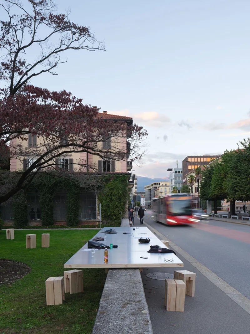 White table with timber benches in a public park beside a roadway at dusk with passing bus