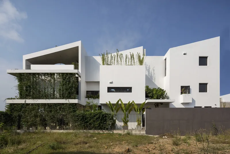 White stucco facade with stacked volumes and planted terraces behind a grey perimeter wall