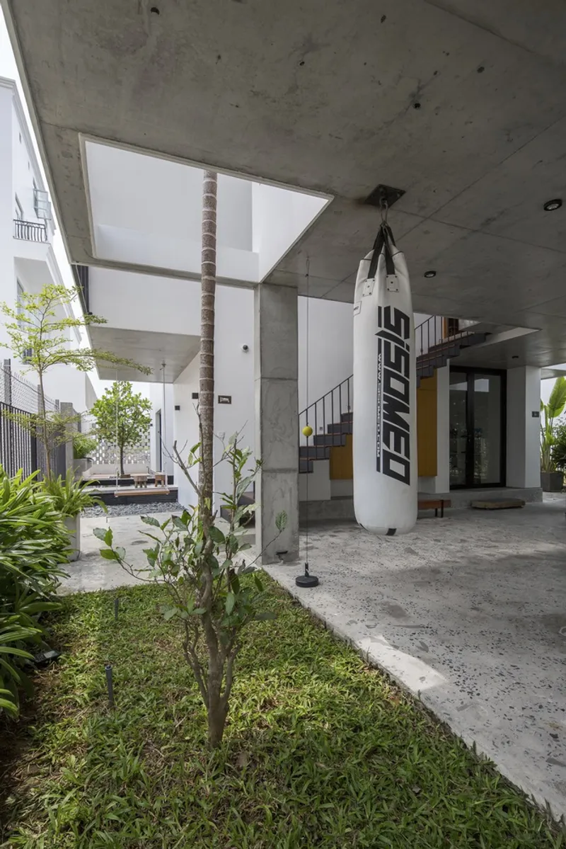 Ground-level courtyard with concrete columns framing a tree and suspended punching bag
