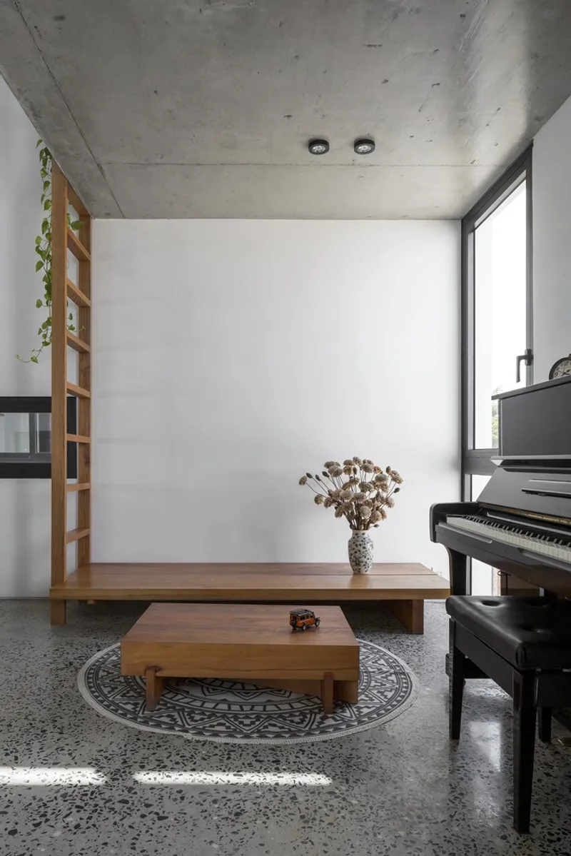 Living room corner with low timber bench, upright piano and circular patterned rug on polished terrazzo floor